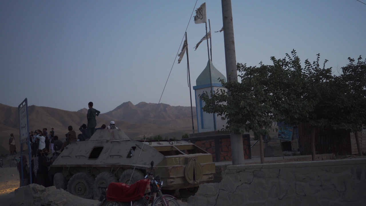 People beside an armoured vehicle and monument with mountains behind